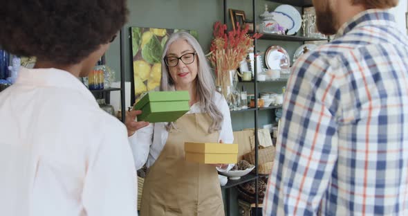 Mature Woman Giving Gift Boxes to Tourists which They Bought in Gift Shop alt