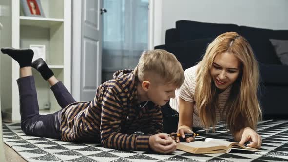 Beautiful Single Mother Helping Her Smiling Son with Homework While Lying on the Floor at Home alt
