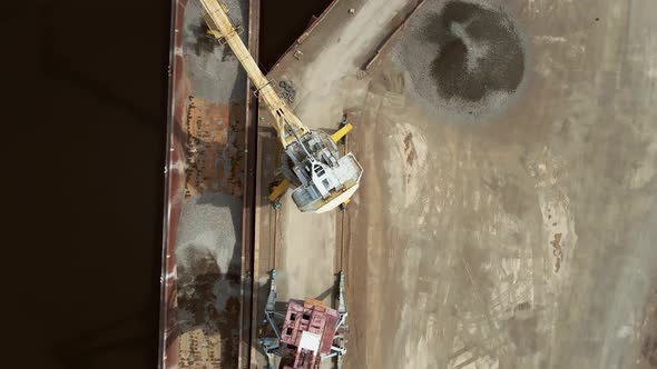 A Large Harbor Crane on the River Bank on the Embankment Unloads a Barge with River Gravel Onto a alt