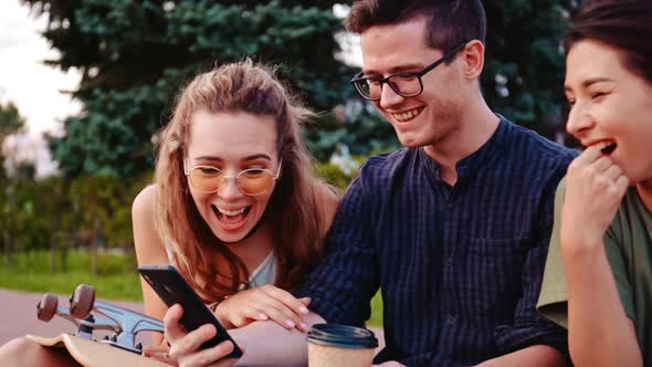 Happy Smiling Teenage Friends Laughing Outside at Something in Smartphone or Mobile Phone