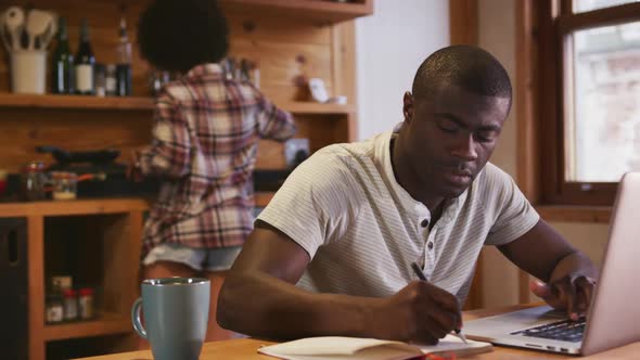 African man working while mixed race woman preparing breakfast alt