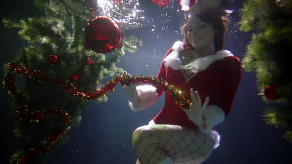 Charming Girl Is Wearing Red Bodysuit with White Fur and Fishnet Stockings Is Floating Underwater alt