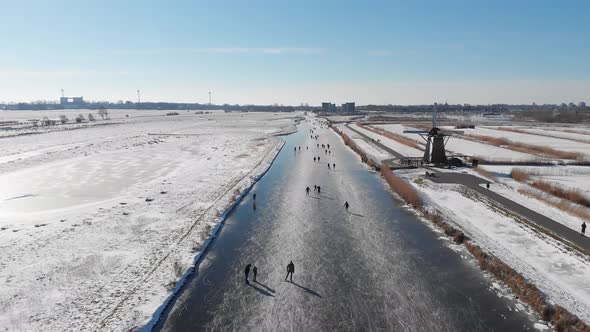 Ice skating on canals in Netherlands beside traditional windmills, aerial view alt