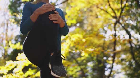 Woman Does Knee To Chest Exercises in Autumn Forest Closeup