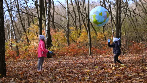 Two girls in medical masks play in the autumn Park with a large inflatable ball. 