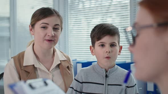 Smiling Mother with Little Boy Visit Therapist Close Up Female Doctor Pediatrician Make Notes in