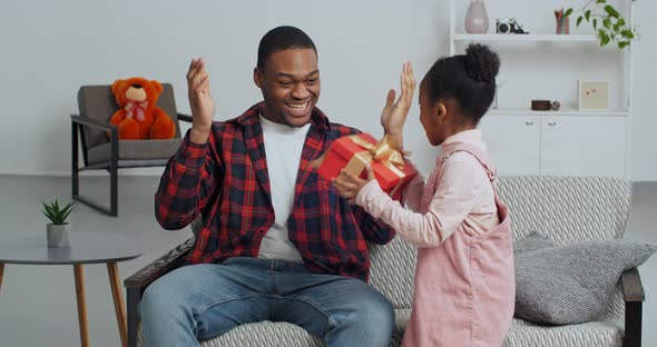 Cute Faro Kid Daughter Make Surprise Present for Dad Receive Gift Box Sit on Sofa Black Man Father alt