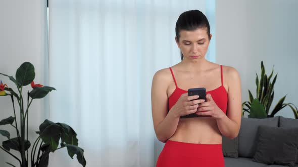 Portrait Athletic Fit Fitness Woman Uses Smartphone at Home in Living Room alt