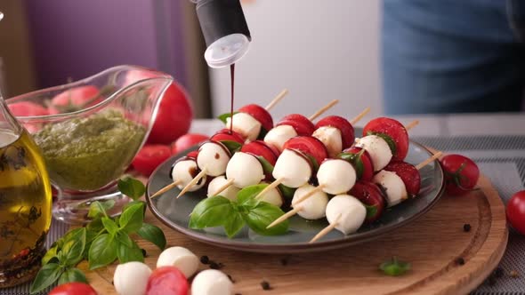 Pouring Balsamic Sauce on Caprese Canapes with Cherry Tomatoes and Mozzarella Cheese Balls alt
