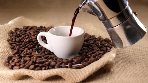 Pouring coffee cup from moka coffee machine on jute and  coffee beans alt