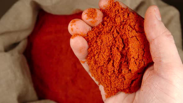 Human hand holds handful of red pepper powder over a sac and throws it