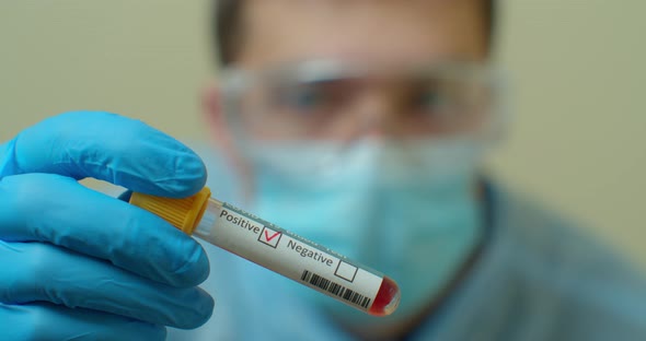 Competent Medical Worker in Protective Uniform Holding Test Tube with Blood for Analysis on COVID 19 alt