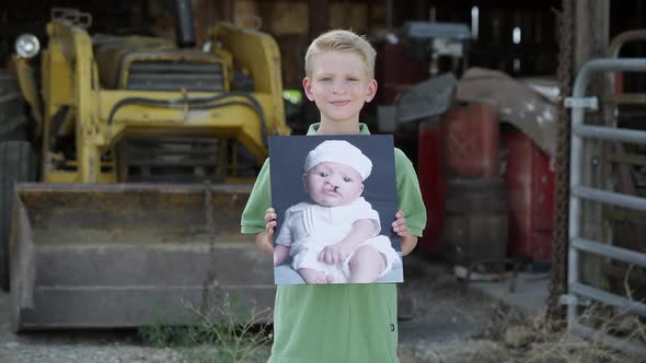 Slow motion of boy showing photo of himself as baby with cleft palate. alt