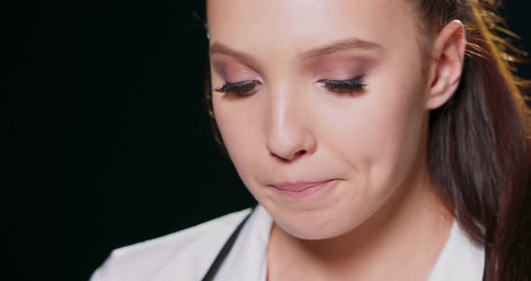 Closeup on the Face of a Worried Young Woman Against a Black Studio Background with Copy Space alt