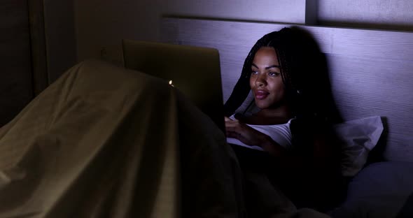 Black Woman using laptop in bed at home. alt