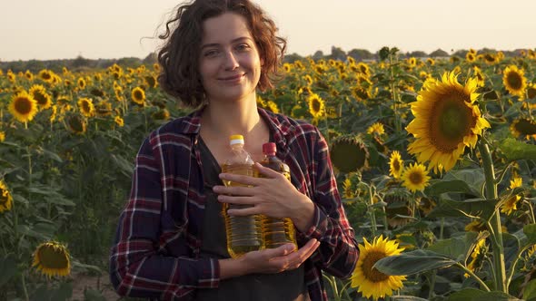 Portrait Of Brunette Woman Holding Bottles Of Sunflower Oil, Standing Against Flowers Of Sunflower alt