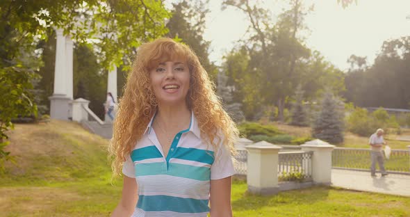 A Happy Blonde Woman Dances and Sings in the Park at Sunset alt