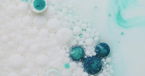 Blue and white bubbles in floating in transparent liquid. A chemical gets poured into the liquid, bu alt