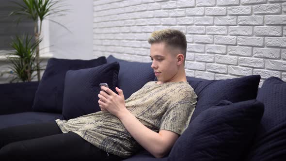 Young Man Using Smartphone Surfing Internet Relaxing on Couch at Home