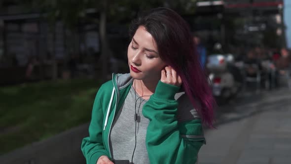 Attractive Young Woman with Colored Hair Enjoying Music in Earphone Using Smartphone and Walk alt