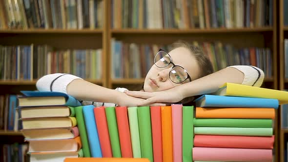 Girl Takes Off Glasses After Reading a Book. A Girl Lies on Books in the Library