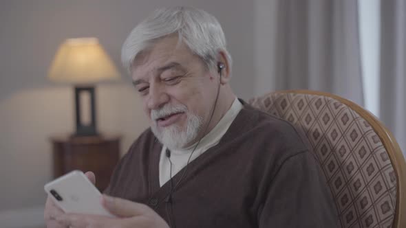 Portrait of Positive Mature Man Moving and Singing As Listening To Music in Earphones. Old Caucasian alt