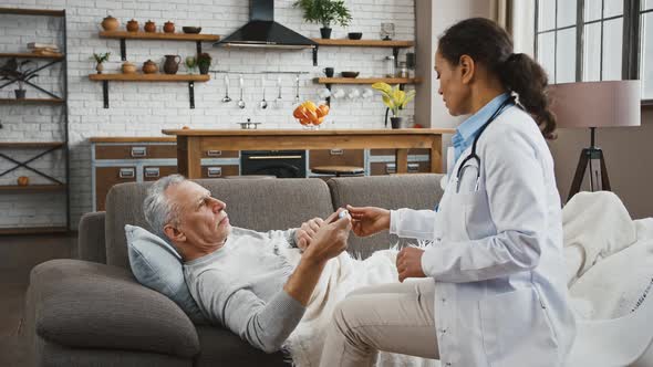 Aged Male Lying on Sofa Measuring Temperature Giving Thermometer to Doctor Woman Who Saying That He alt