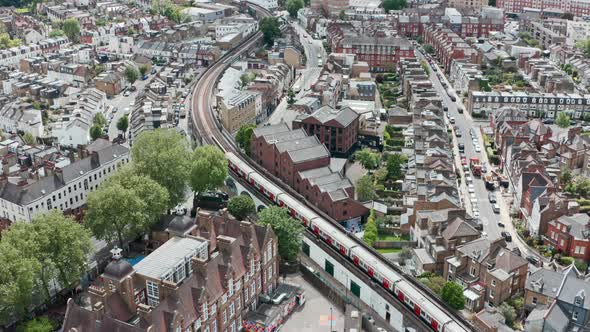 Cinematic drone follow shot of district line train winding through residential London Putney bridge alt