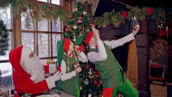 Funny elves with Santa indoors. Christmas decorated room and Santa Claus alt