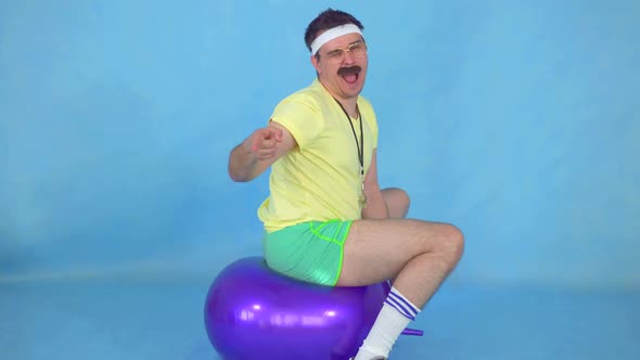 Funny Man Coach with a Mustache From 80's on the Fitness Ball on Blue Background alt