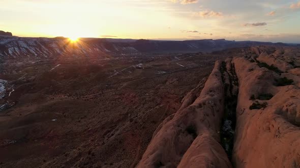 Flying over red rock cliffs as the sun sets in the distance alt