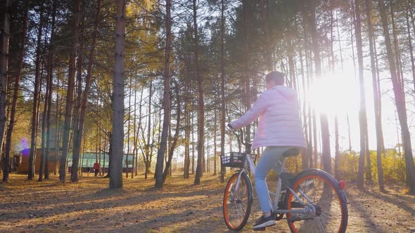 Slow Motion Young Woman Riding Bicycle in Autumn Coniferous Forest at Sunset