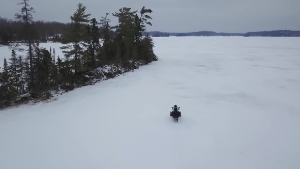 Aerial View over Frozen Lake Following Snowmobile Rider in Winter 4