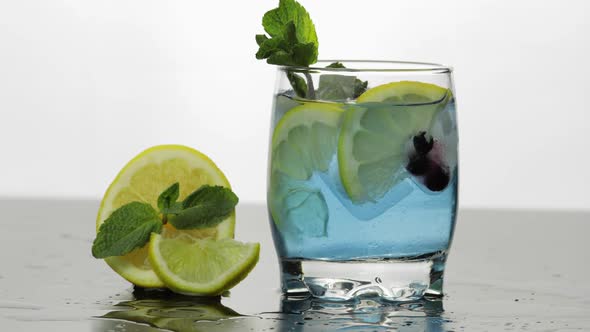 Adding Leaves of Mint in a Glass with Cold Drink, Lime, Lemon, Currants, Ice alt