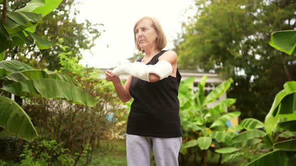 Senior Elderly Woman Doing Exercises and Gymnastic for Hand with Injury Broken Arm in Cast Outside