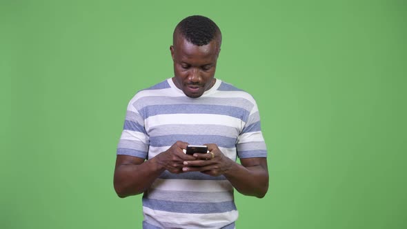 Young Happy African Man Smiling While Using Phone alt