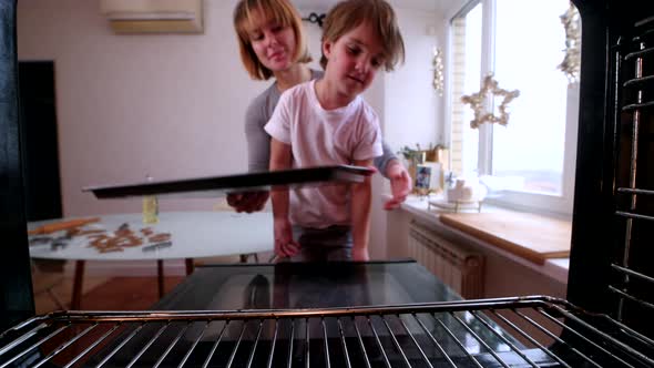 Young Mom with Red Short Hair and Blonde Son Put Homemade Gingerbread Cookies in the Oven alt