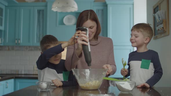 Kids helping mother to knead the dough with blender alt