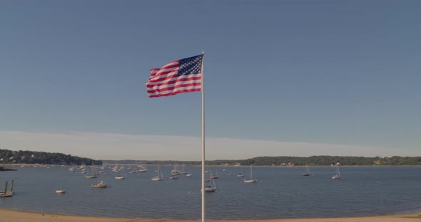 Aerial Pan of an American Flag at a Memorial Park and Boats Anchored at Harbor alt