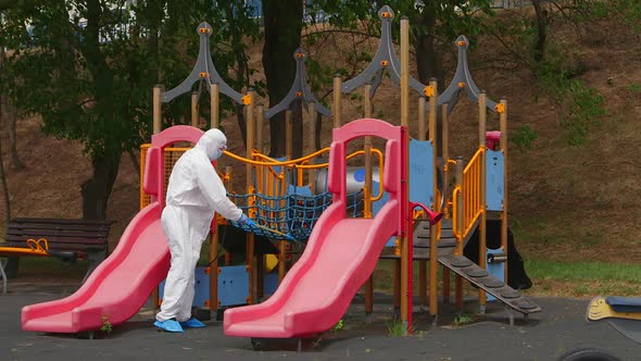 Close frame on the swing. Man wearing protective suit disinfecting the bank with spray chemicals