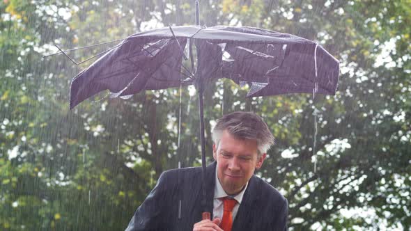 Businessman Sheltering Underneath a Broken Umbrella in the Rain