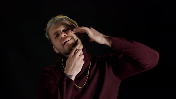 Portrait of Unshaven Young Man in Trendy Stylish Clothes Shaving with Knife Against Black Background alt