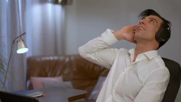 Young Handsome Middle Eastern Man Sitting in Home Office Listening to Music in Headphones alt