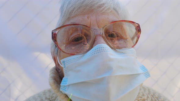 Portrait of Granny Wearing Protective Mask From Virus. Elderly Lady Looking Into Camera Showing Sad alt