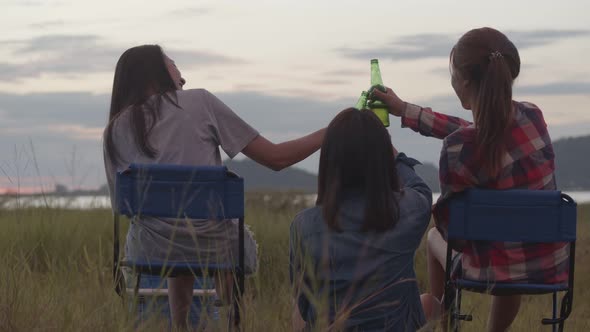 Asian women sitting on a chair with friends camping in nature having fun together drinking beer.