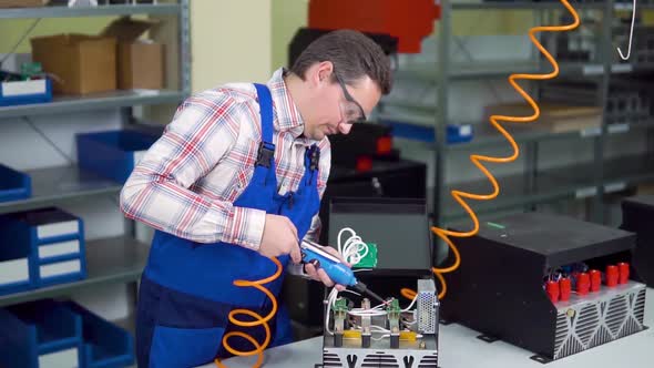 Young Worker in Shirt and Overalls Assembles Electronic Components in a Hi Tech Factory alt