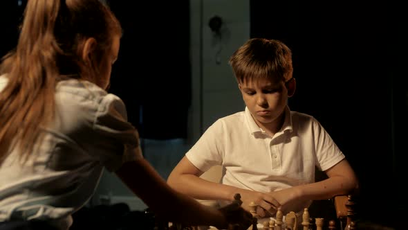 Young boy in white polo playing chess with classmate at competition