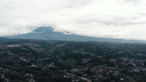 Cinematic aerial view of a mountain with white clouds surrounds it in a rural area.