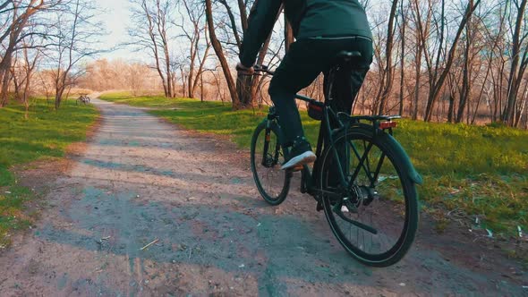 Young Guy Rides a Bicycle Along a Path in a Green Forest Rear View in Slow Mo alt