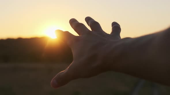 Male Hand Against Sunset. Touch the Sun. Sun Shines Through Fingers. Slow Motion alt